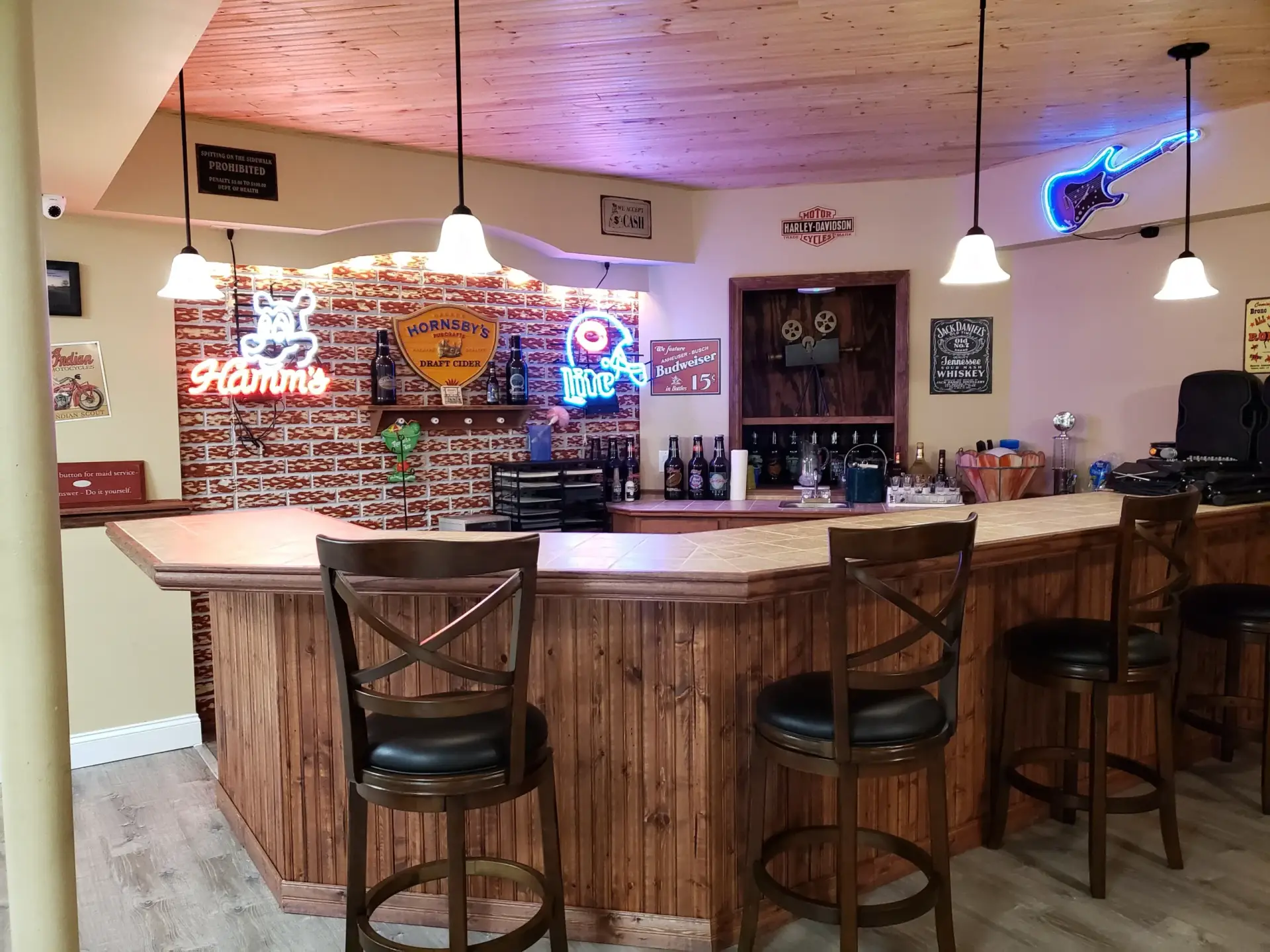 Wooden bar with high stools in a cozy pub, brick accent wall, neon signs, and bottles lined on shelves behind the bar.