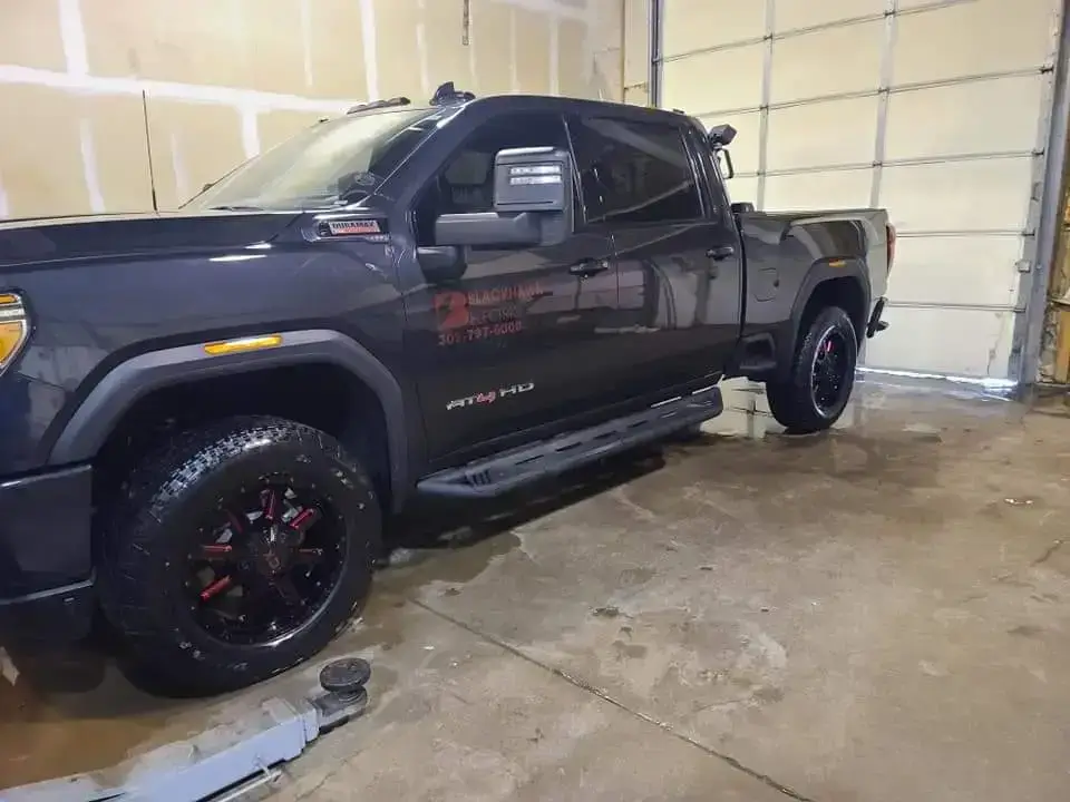 Dark gray/black crew-cab pickup truck with large off-road tires parked inside a garage; wet floor and tools visible nearby.