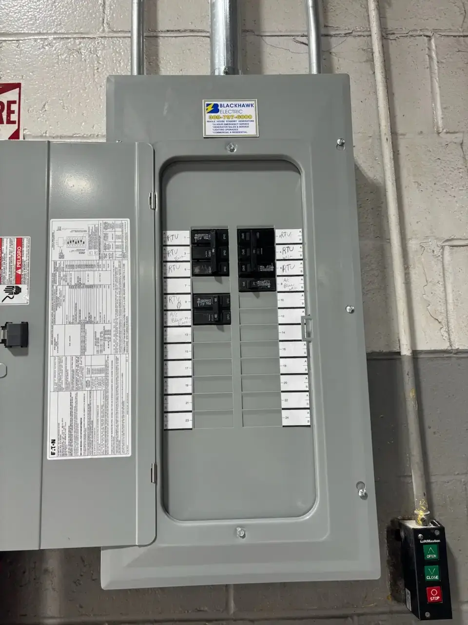Industrial electrical breaker panel mounted on a concrete wall, with labeled circuit breakers and a utility control box to the right.