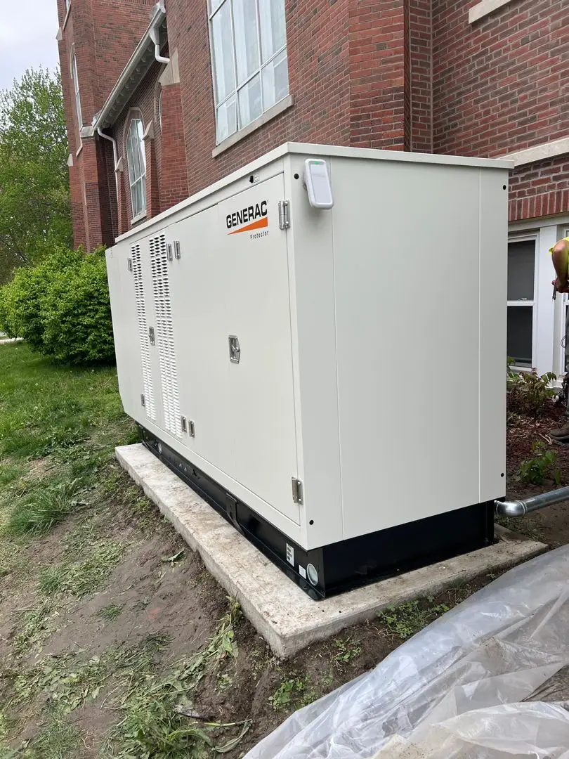 White Generac standby generator on a concrete pad beside a brick building, with vent panels and access doors visible.